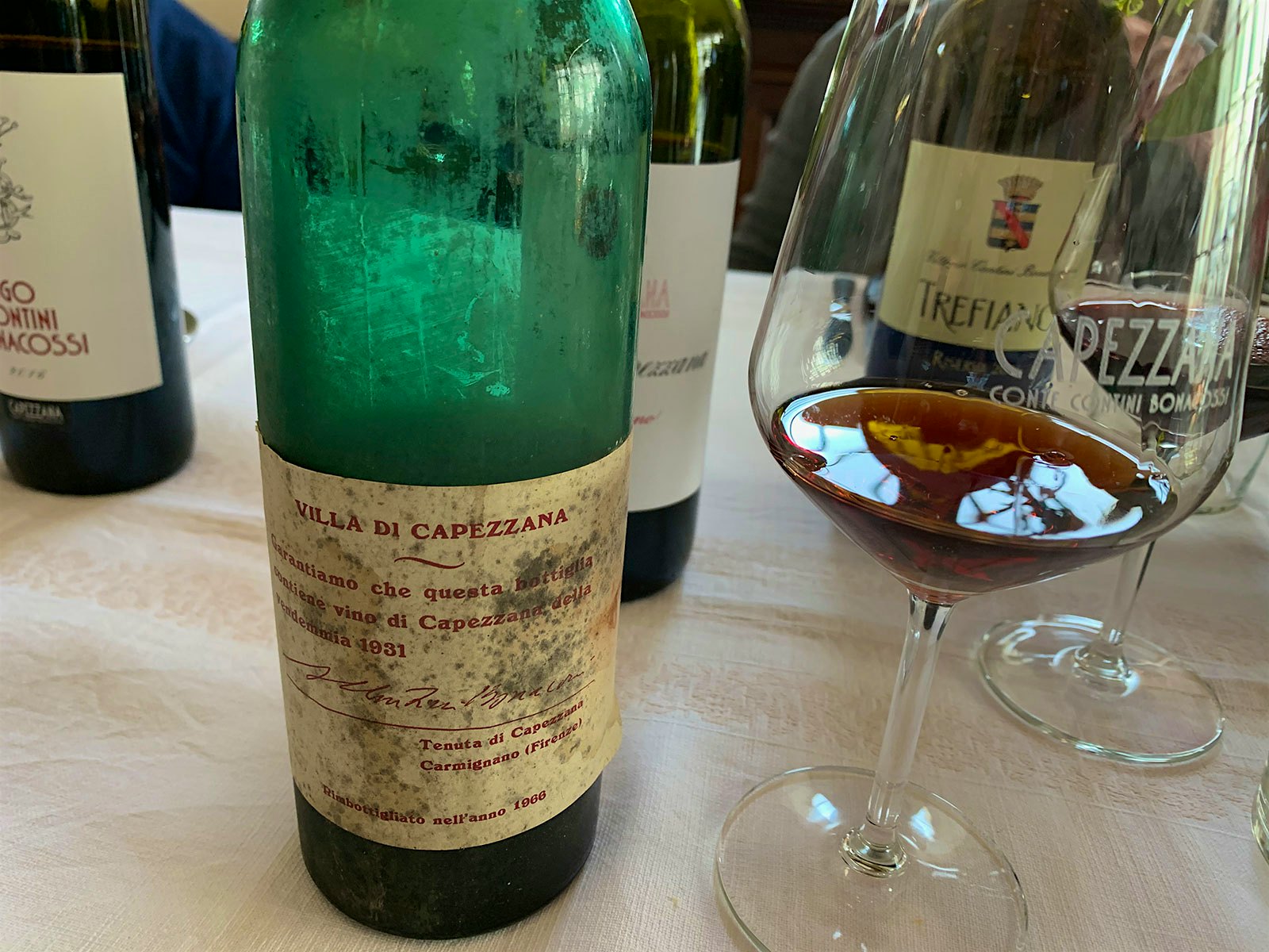 A bottle of 1931 Villa di Capezzana Carmignano next to a glass holding the amber-colored wine